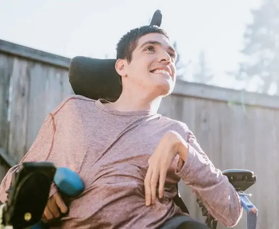 A disabled boy in a wheelchair smiling at being able to freely go outside thanks to disability tech