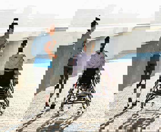 A woman is a wheelchair accompanying her friend who is jogging because it is an accessible environment.