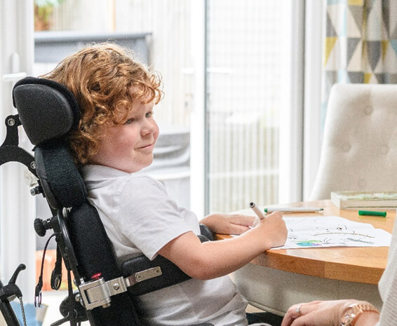 A healthcare worker encouraging a disabled boy to colour during a therapy at home session.